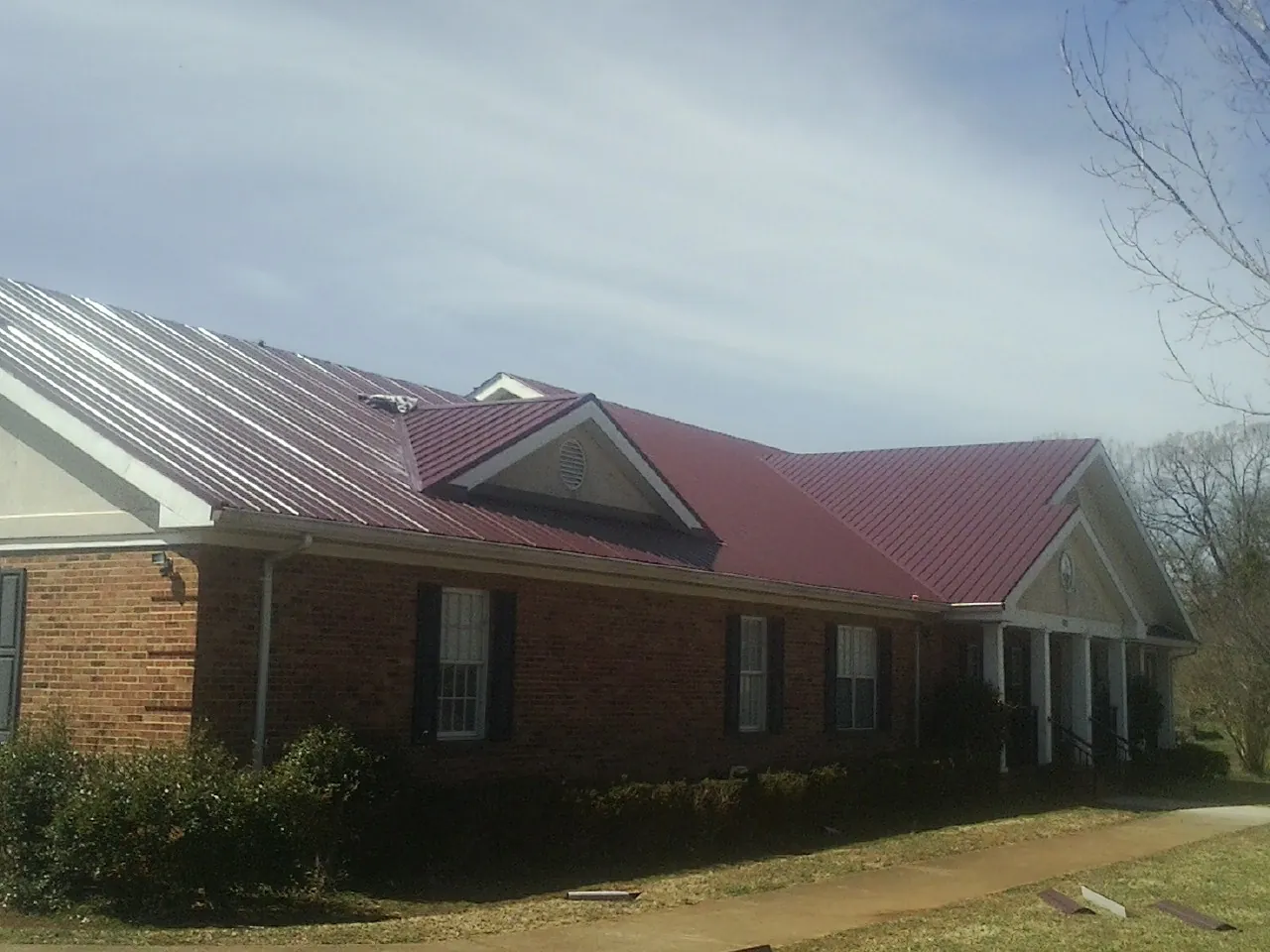 Red metal roof with gabled entries on a long brick building, from a Hail Damage Roof Repair job in Summertown