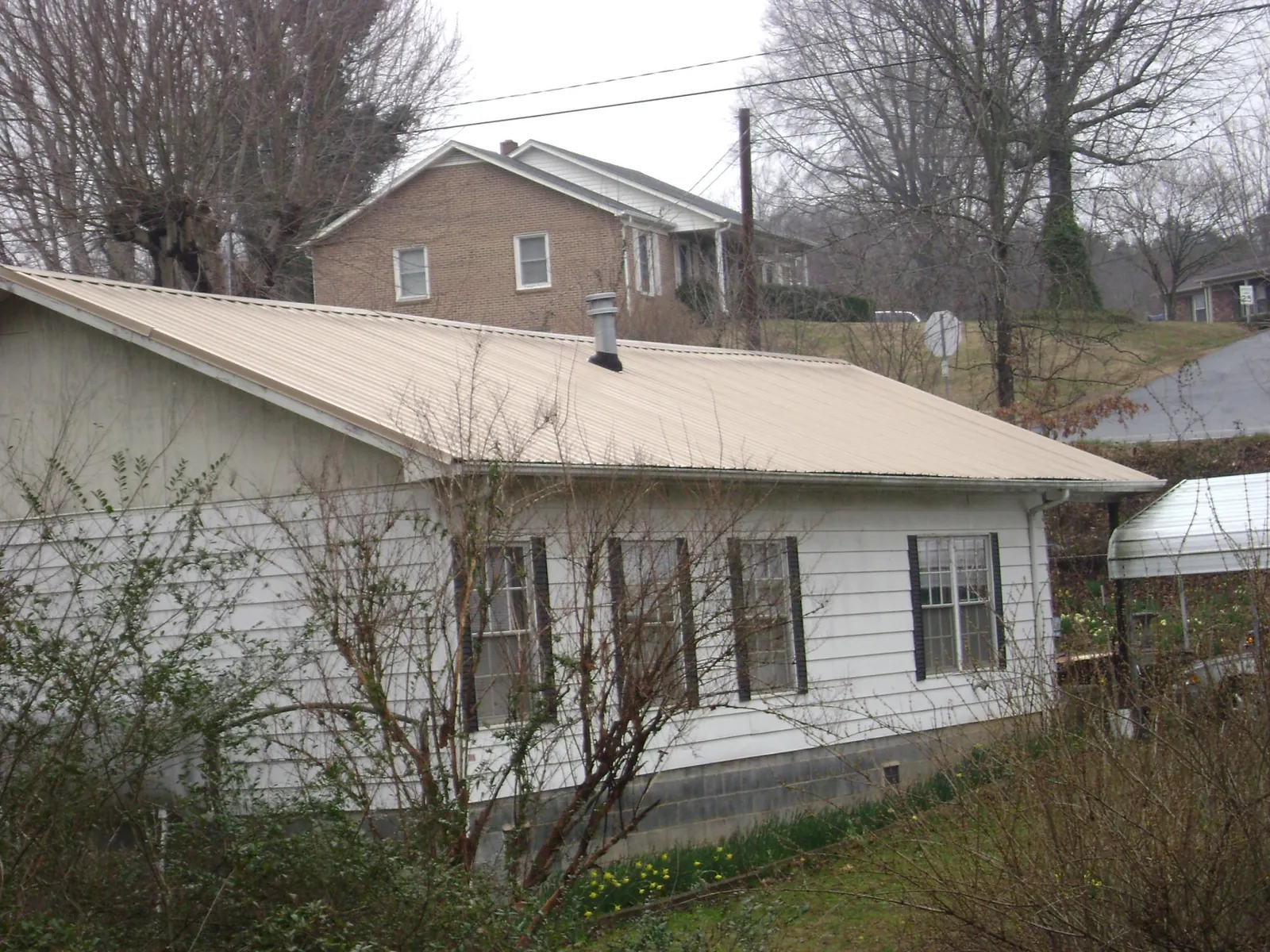 Tan metal roof on a white sided house set into a hillside — Commercial Roofing by Roofing Brothers in Summertown